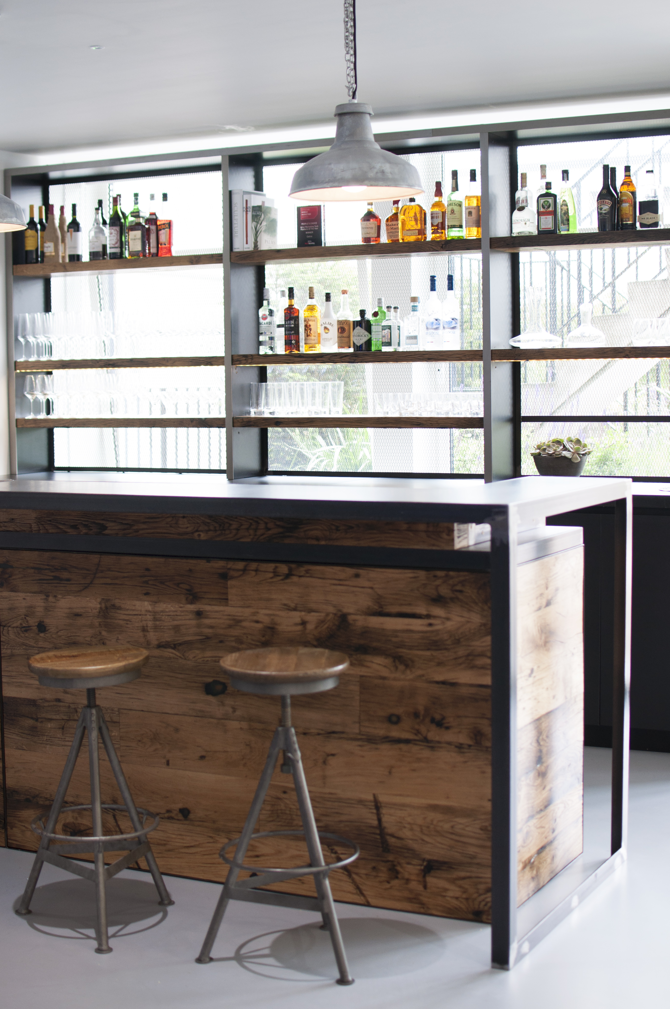 Wooden bar with stalls and glass shelving displaying alcohol and glasses