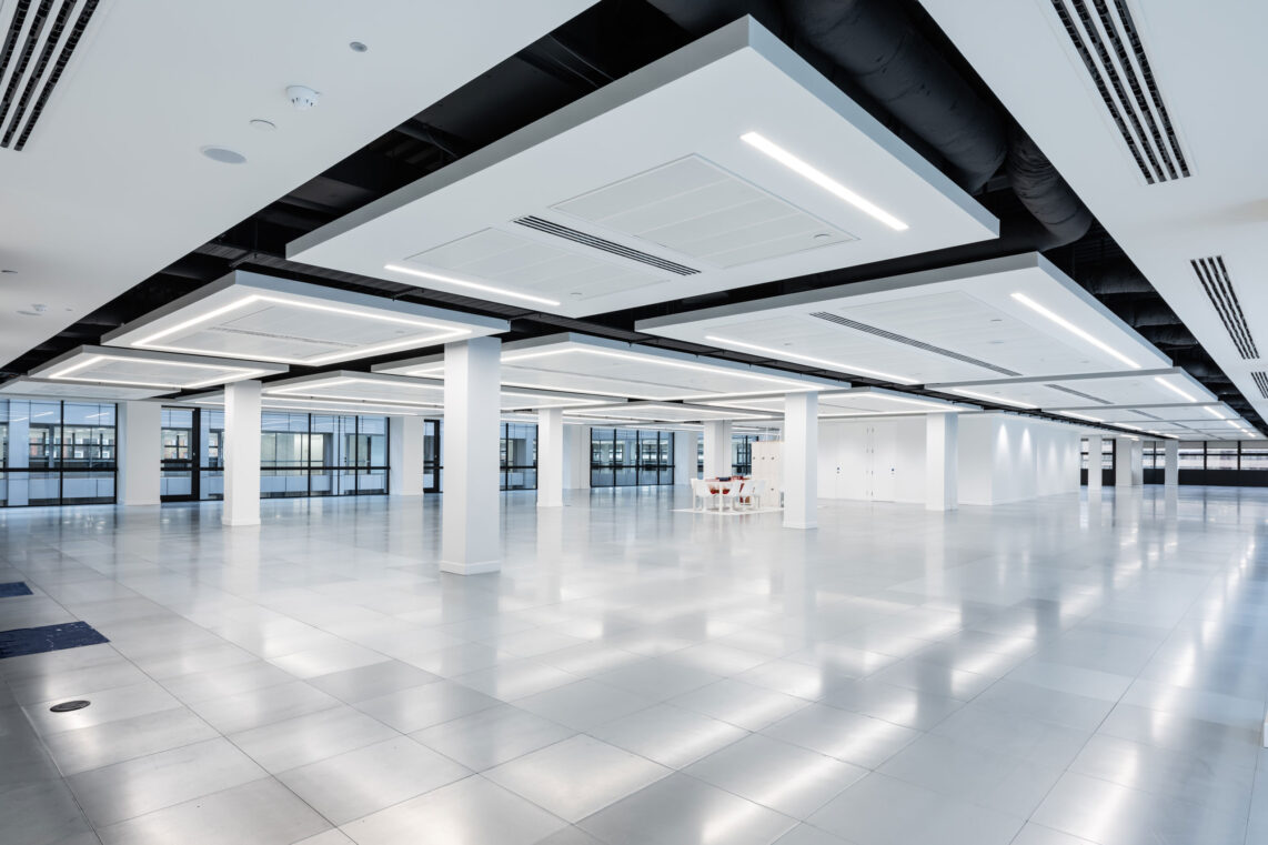 A clean well-lit office space clear of furniture. The square lights in the ceiling reflecting off of the tiled floor